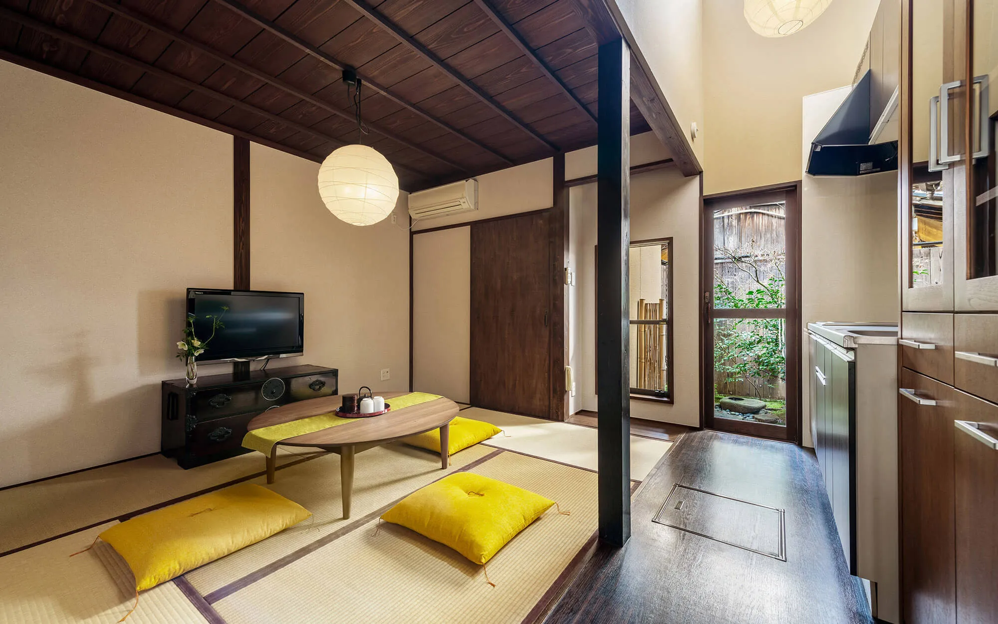 A townhouse living room: low table and floor cushions on tatami, sliding doors open to the kitchen and entrance